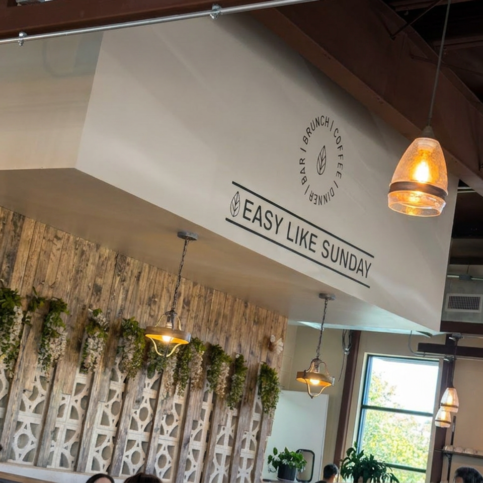 Warmly lit restaurant interior with wood paneling, hanging plants, pendant lights, and “Easy Like Sunday” brunch and coffee signage.