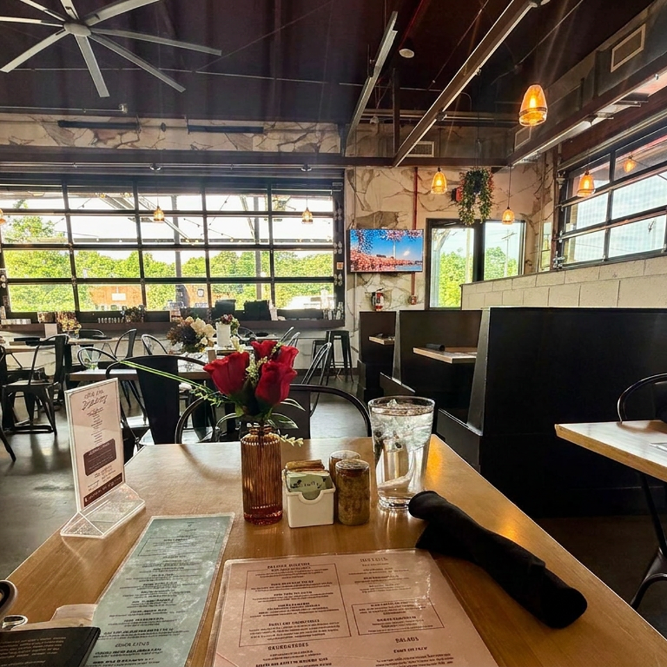 Bright modern restaurant dining room with large windows, black booths, wooden tables, menus, red roses, and pendant lighting.